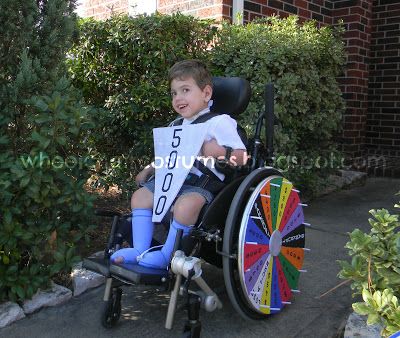 Boy in wheelchair with Wheel of Fortune wheel on his wheel covers. He is holding a $5000 wheel piece.