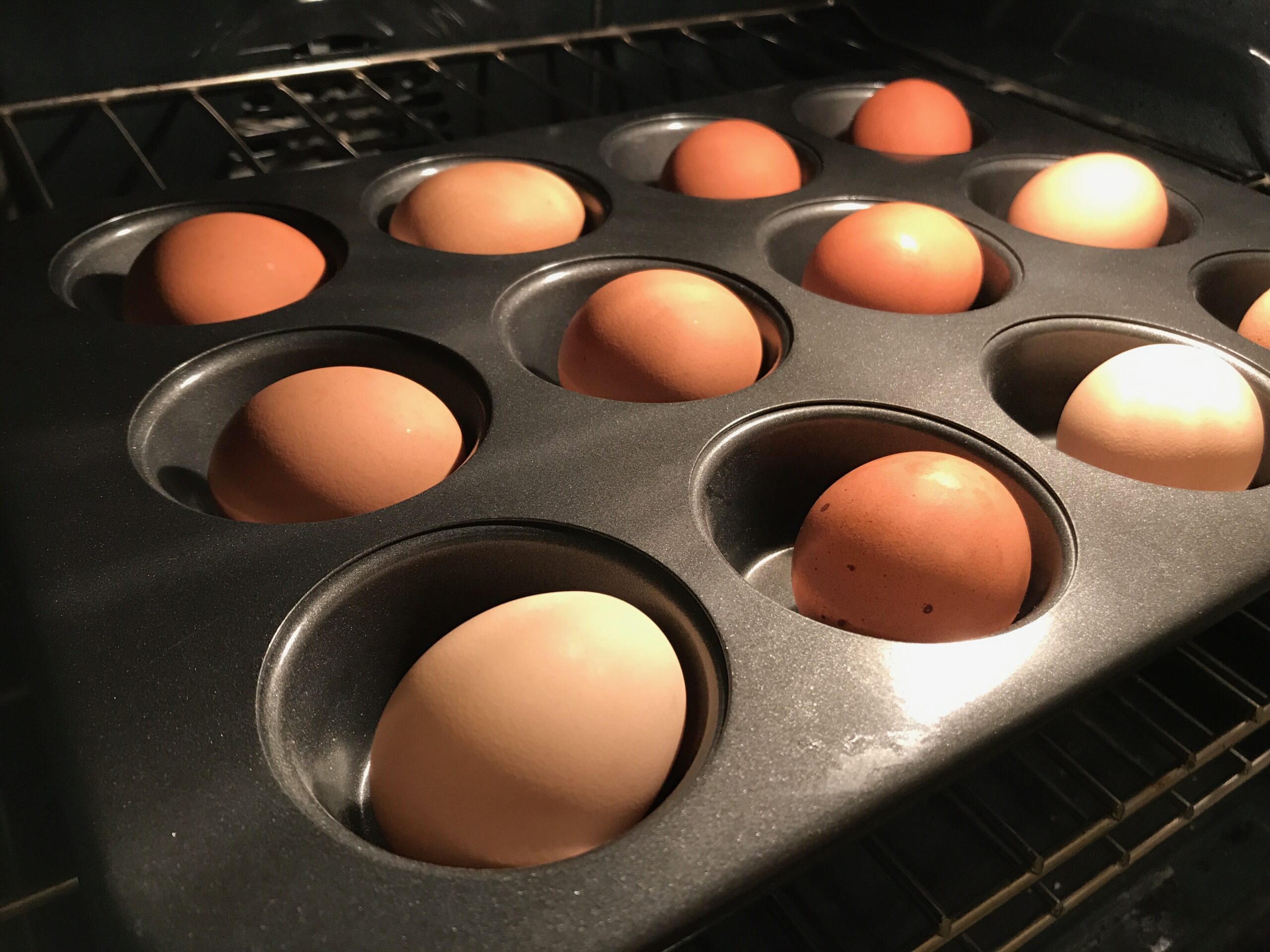 Whole eggs in a muffin pan, inside of an oven