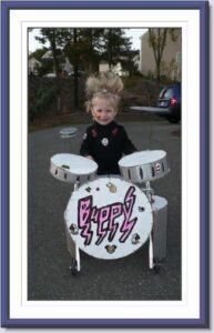Girl with punk rock hair stands behind a drum set that is attached to her walker.