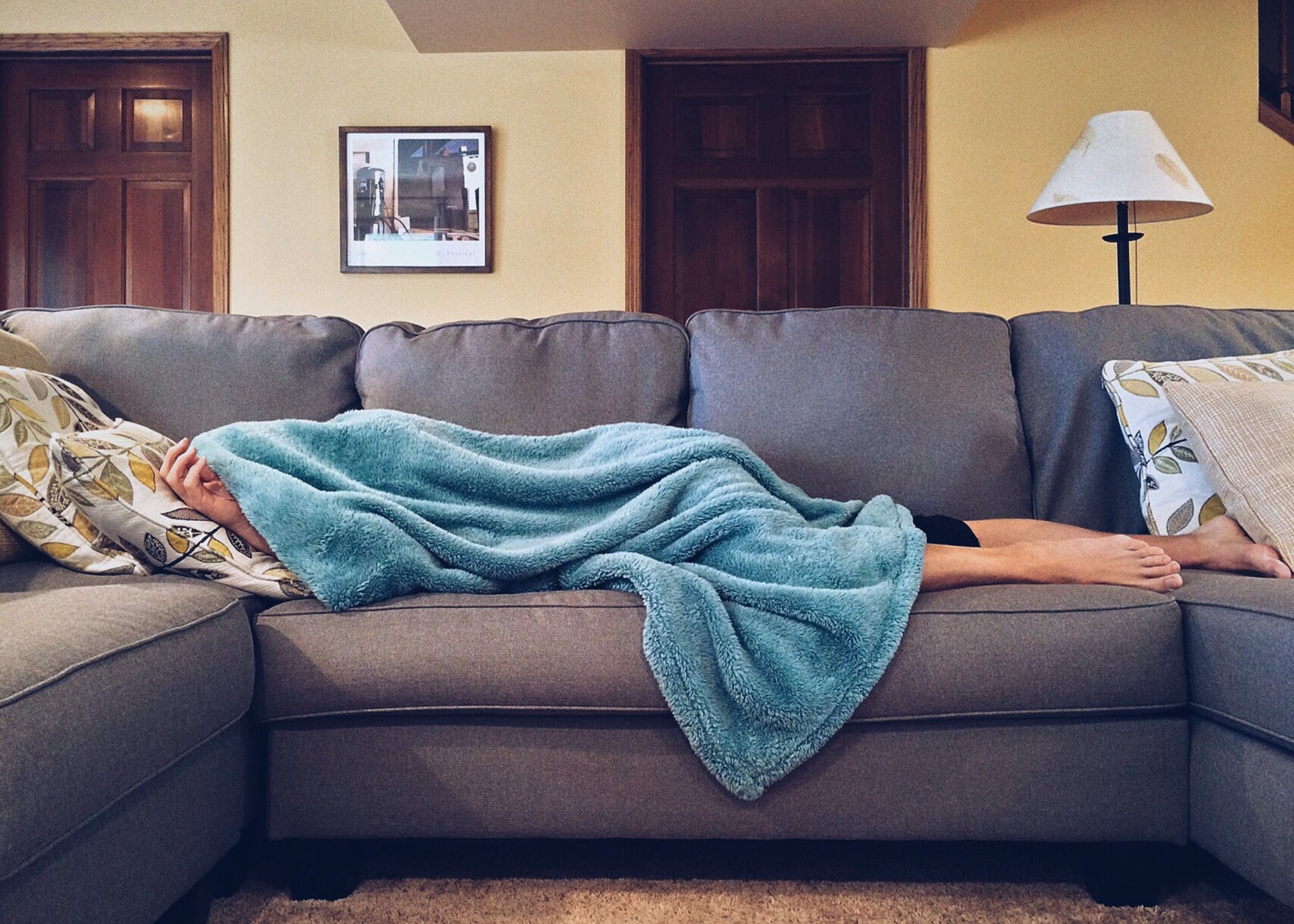 Person laying on a couch with a blanket covering their head and most of their body