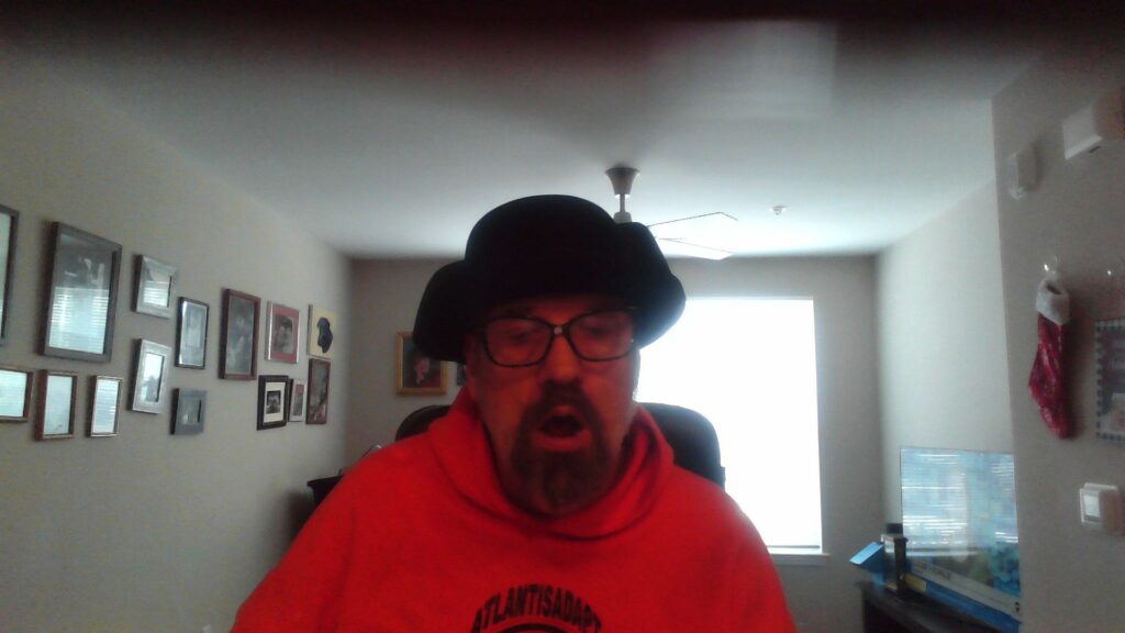 Male with a beard, wearing a brimed hat, with wonderful glasses, and a bright orange sweatshirt